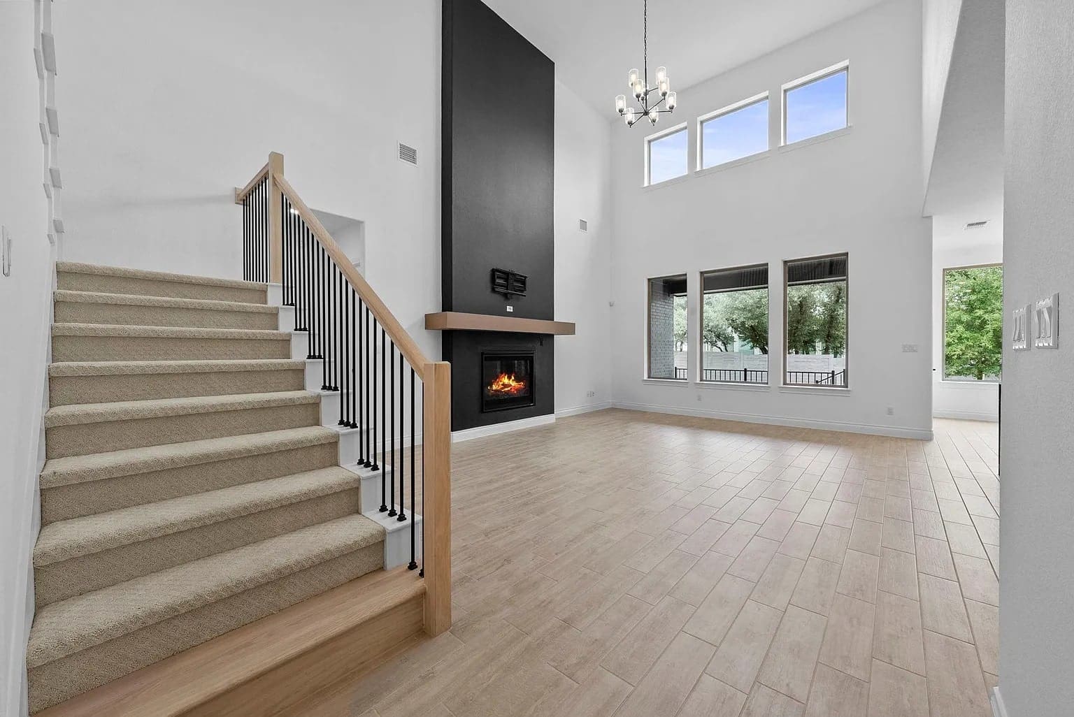 Spacious living room with high ceiling, fireplace, staircase, and large windows.
