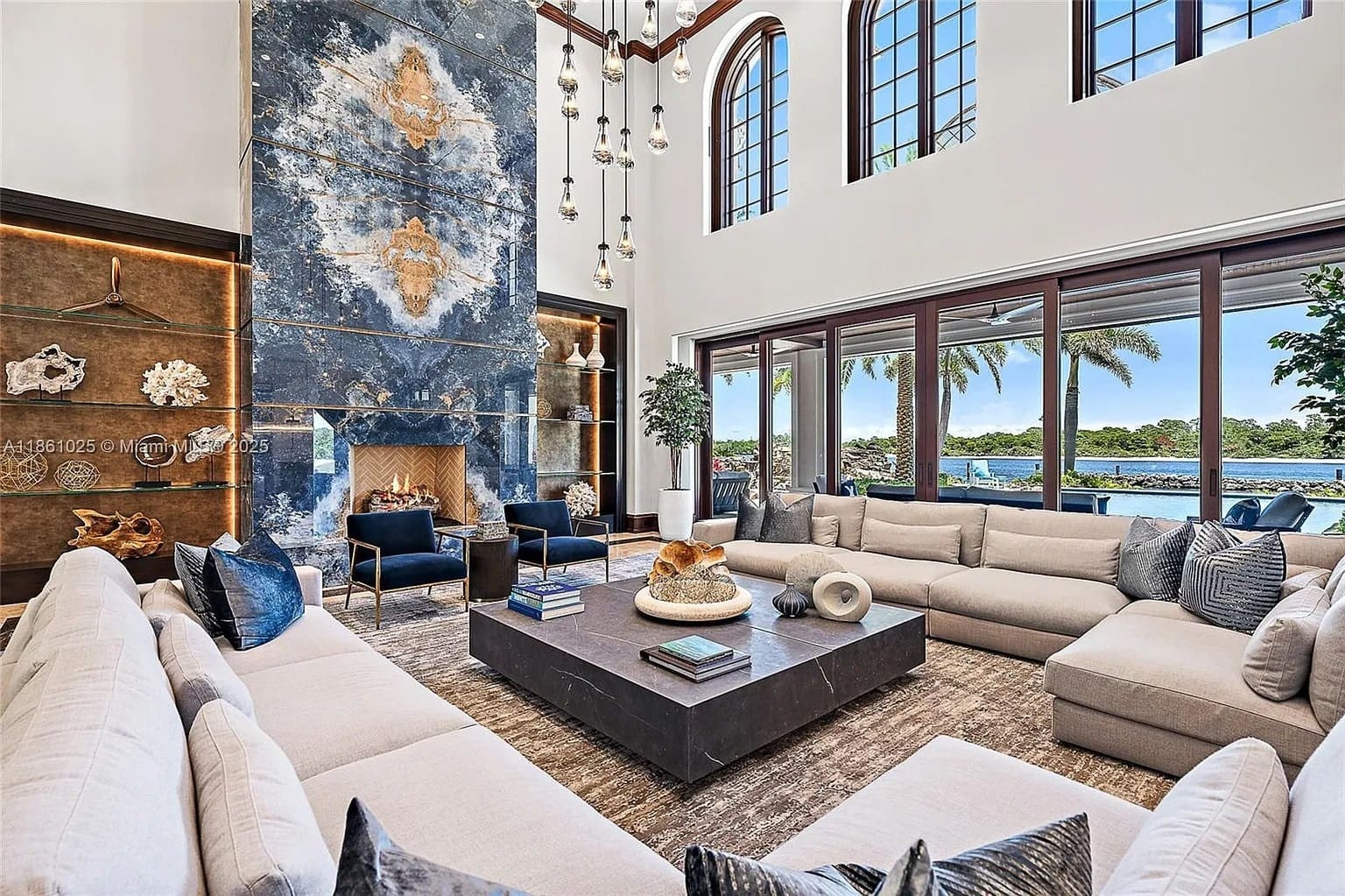 Luxurious living room with large windows, modern furniture, and a tall, decorative fireplace.
