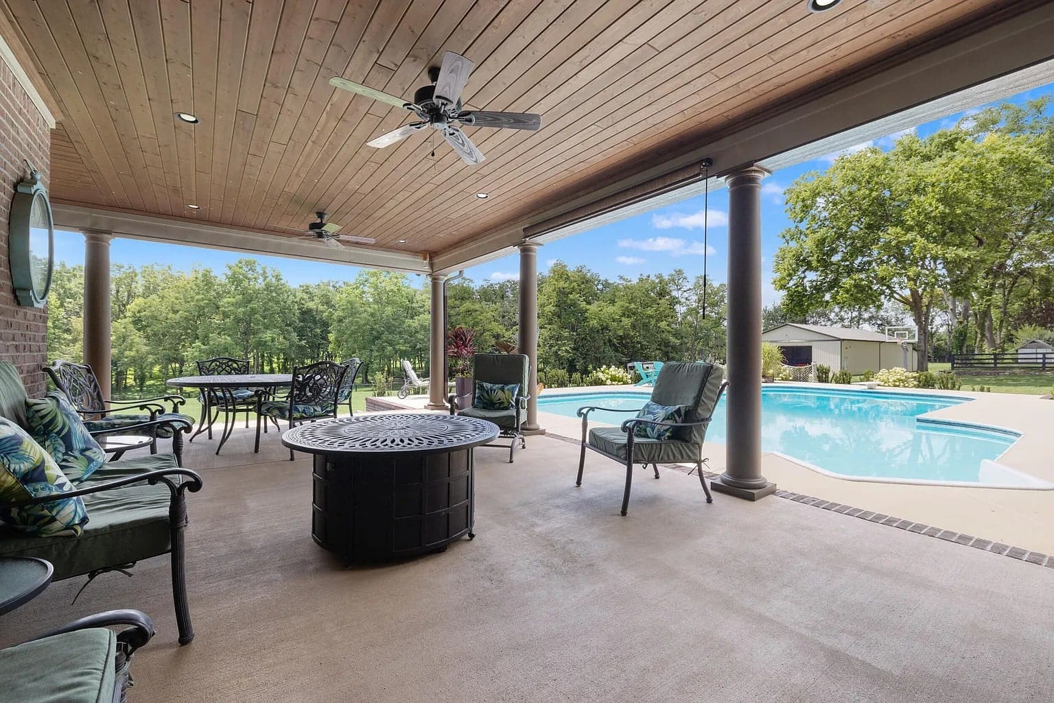 Covered patio with seating and ceiling fans overlooking a pool and lush greenery.
