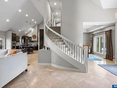 Spacious modern living room with a curved staircase, open kitchen, and large windows.
