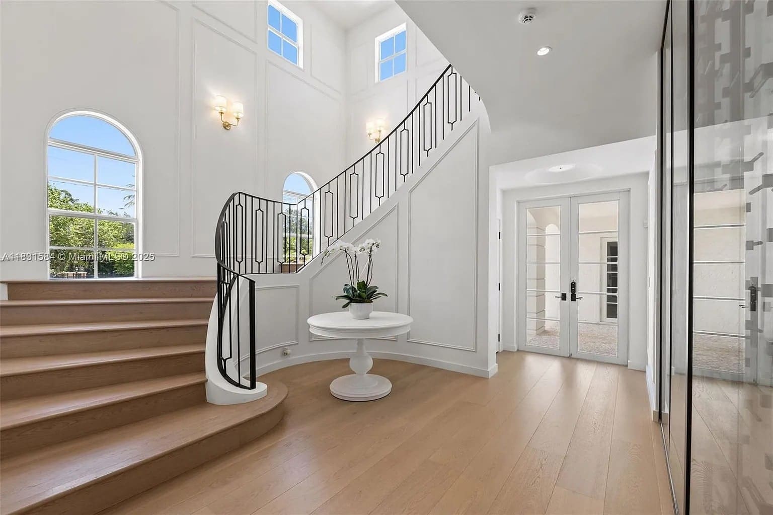 Spacious foyer with curved staircase, wooden floors, and a round table with a plant.