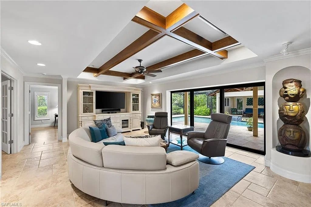 Modern living room with curved sofa, armchairs, TV, and large windows overlooking a pool.
