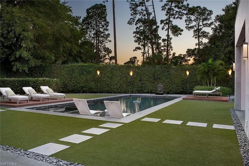 Modern backyard with a pool, lounge chairs, and surrounding trees at sunset.
