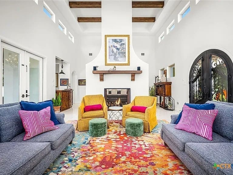 Spacious living room with colorful furniture, high ceilings, exposed beams, and a fireplace.
