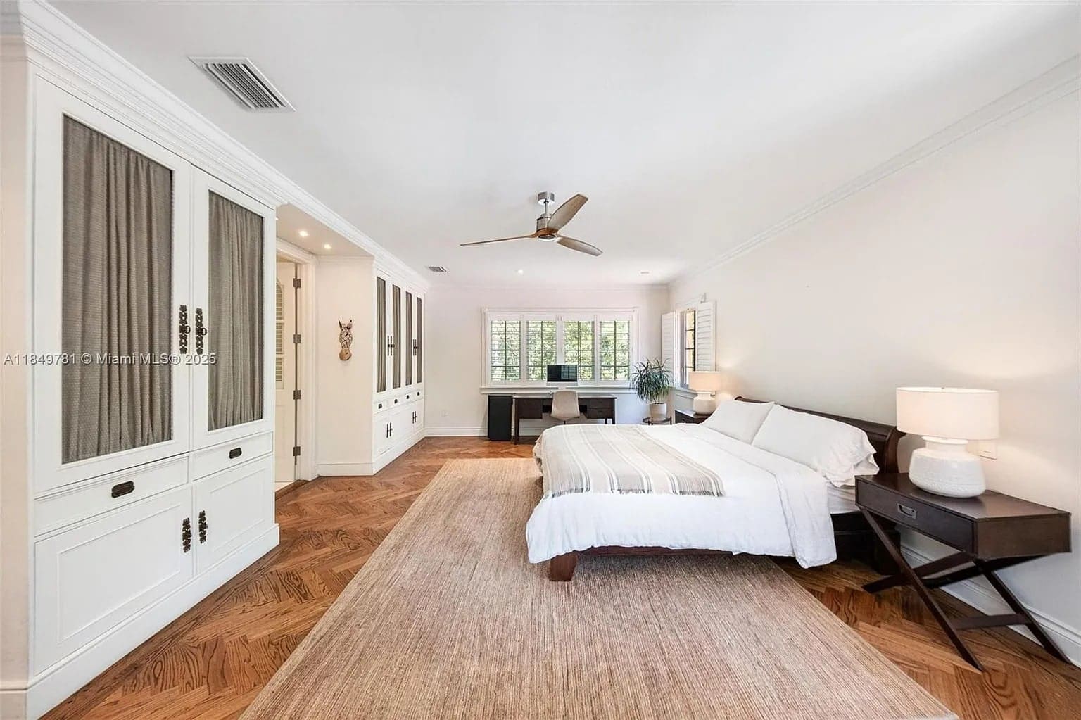 Spacious bedroom with a large bed, wooden floor, built-in wardrobe, and a desk by the window.