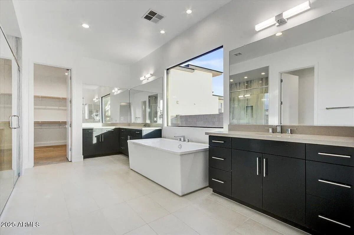 Modern bathroom with large mirrors, dark cabinets, a central bathtub, and a walk-in closet.
