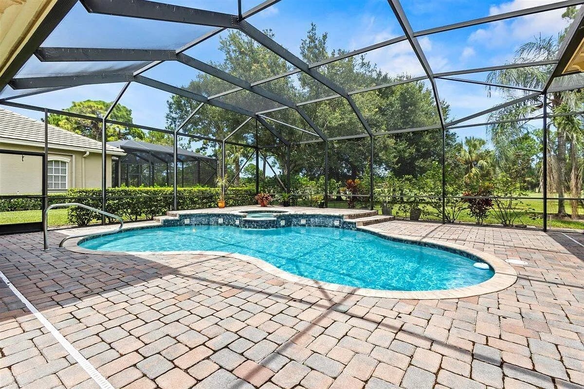 Screened-in backyard pool area with brick patio and surrounding greenery.
