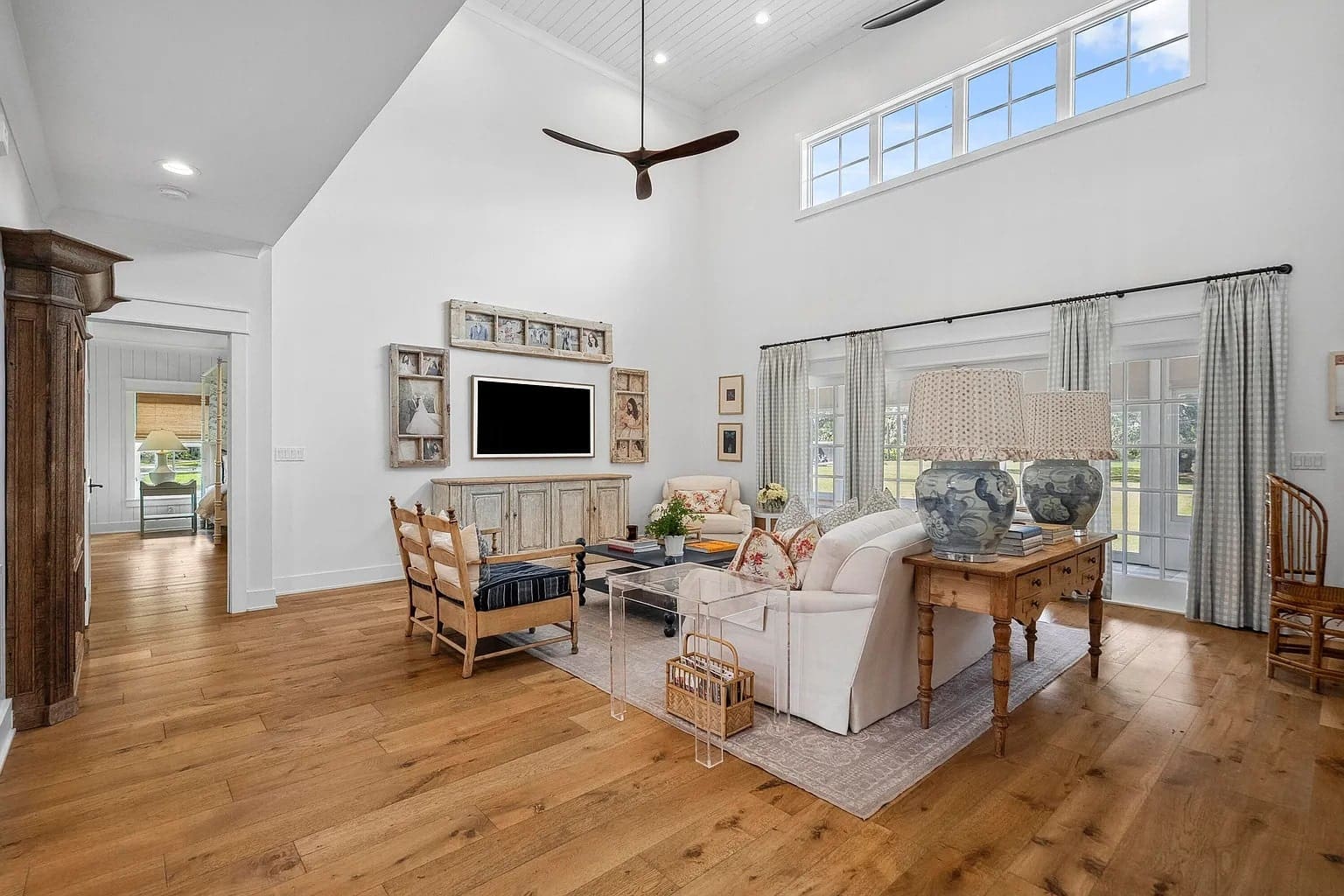 Spacious living room with high ceiling, wooden floor, modern furniture, and large windows.
