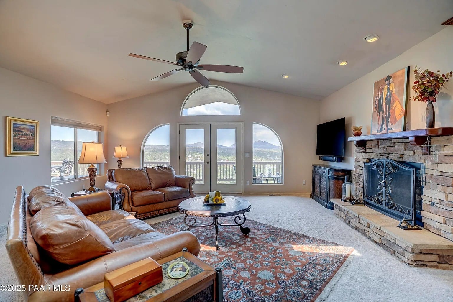 Spacious living room with leather sofas, large windows, stone fireplace, and mountain views.
