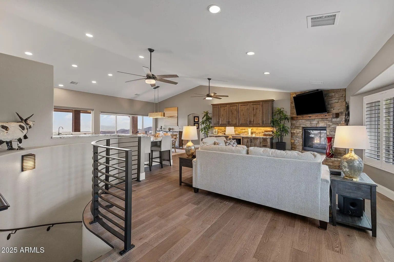 Modern open-concept living room with a fireplace, kitchen, and spiral staircase. Neutral tones and ample lighting.
