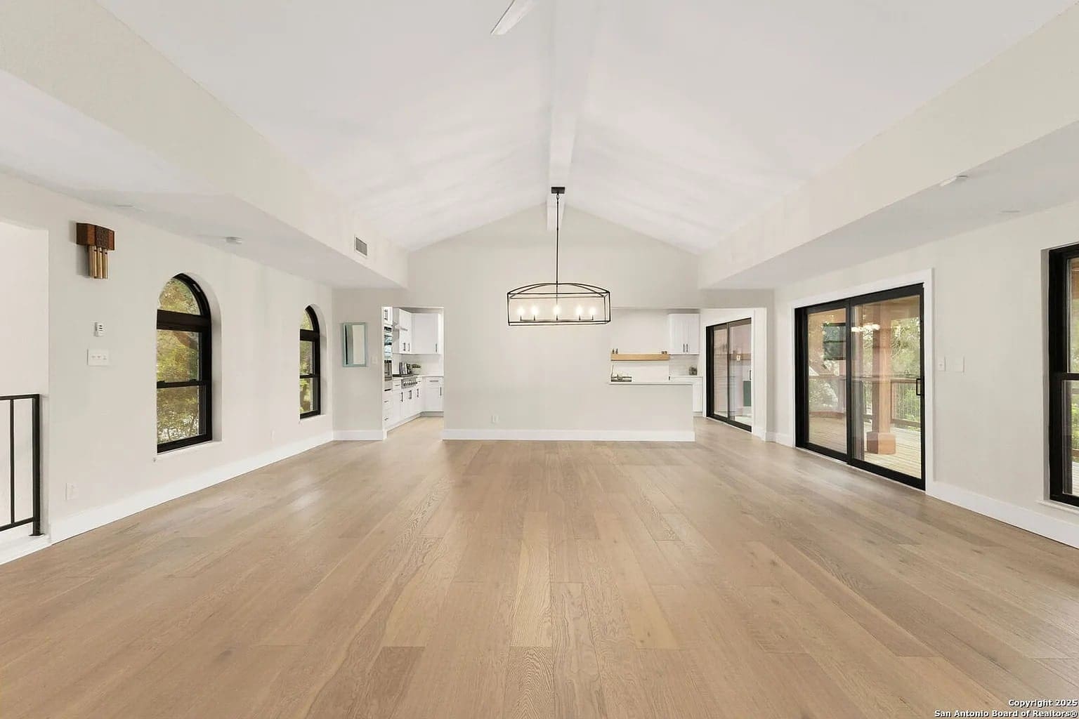 Spacious empty living room with wooden floors, large windows, and view into a modern kitchen.