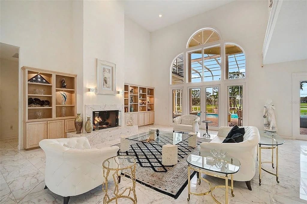 Luxurious living room with high ceiling, large windows, elegant furniture, and a view of a pool.
