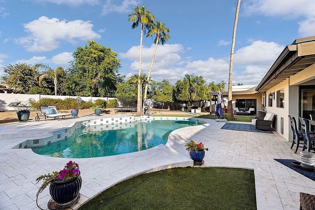 Backyard with a swimming pool, patio seating, palm trees, and clear blue sky.

