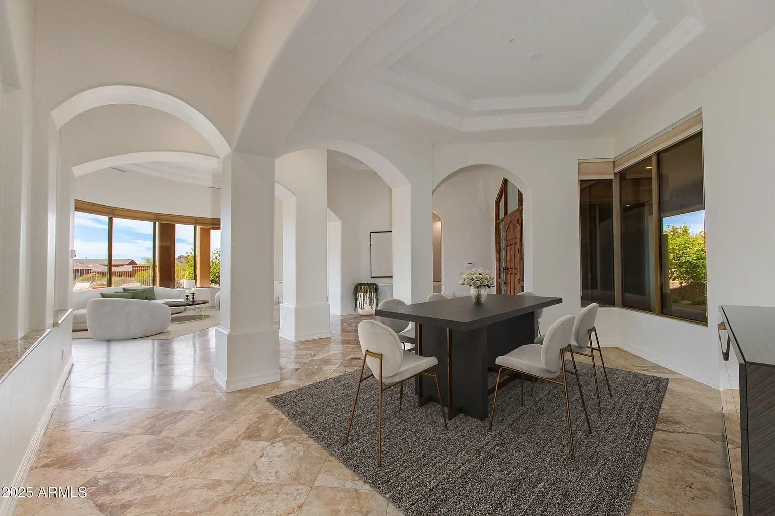 Spacious modern dining area with a dark table, white chairs, and large windows.
