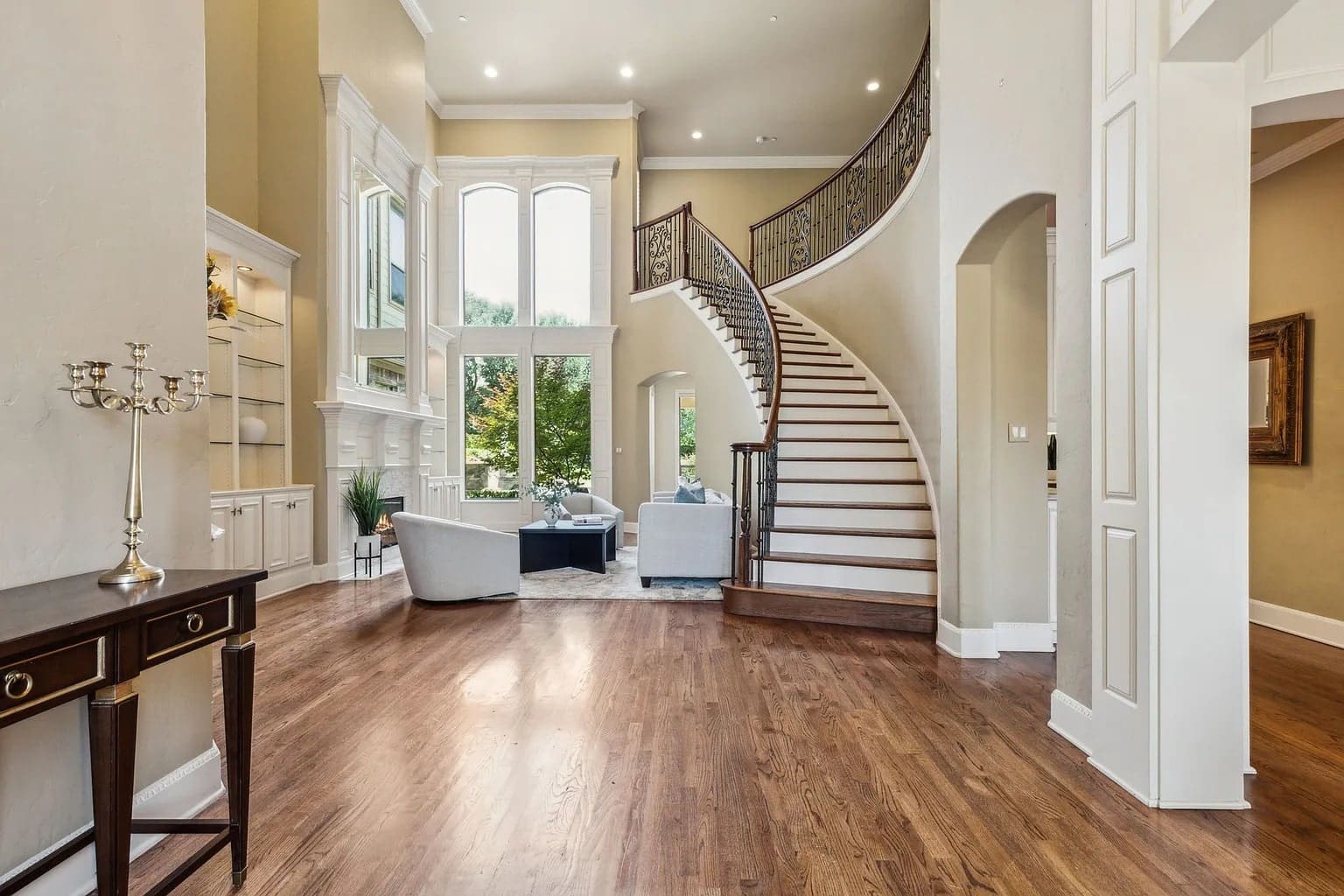 Spacious living room with a grand staircase, large windows, and elegant furniture.
