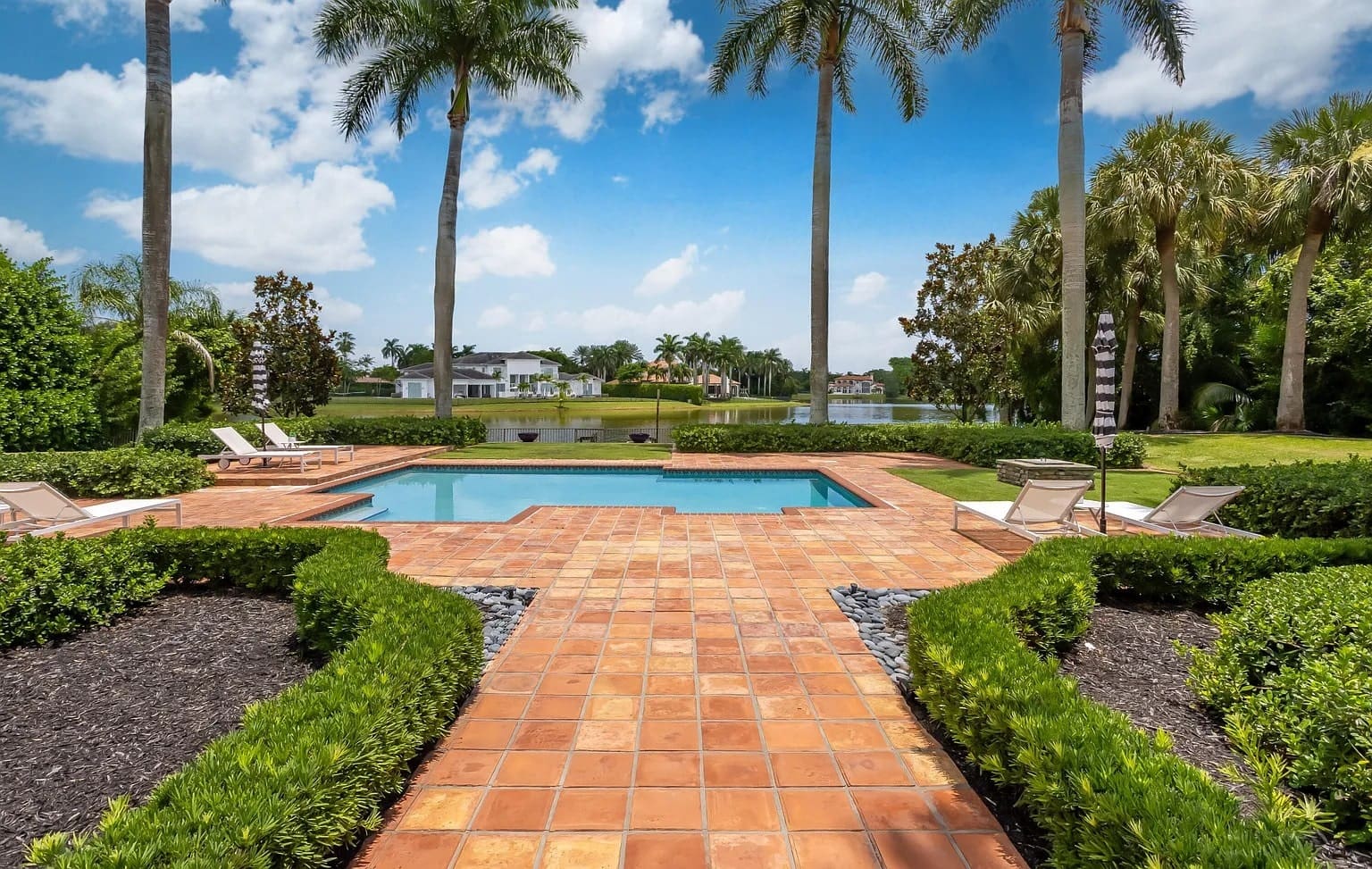 Backyard with a pool, surrounded by palm trees, overlooking a lake and distant houses.