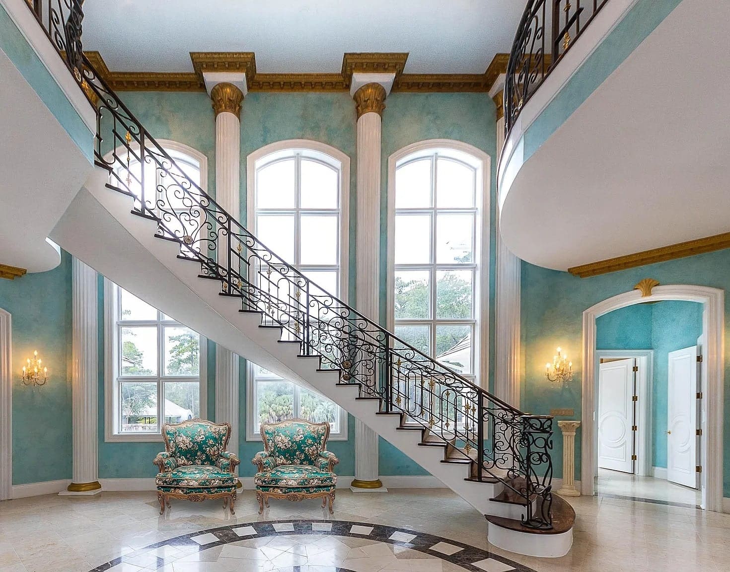 Elegant foyer with a grand staircase, large windows, and ornate furniture in a luxurious setting.
