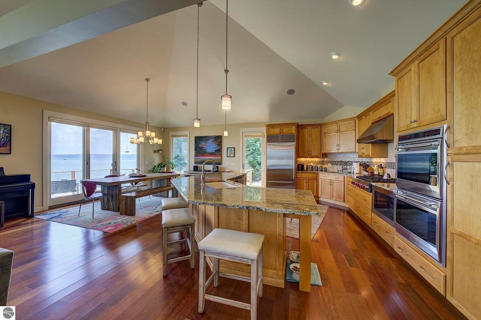 Spacious kitchen and dining area with wooden cabinets, island, and large windows overlooking a lake.
