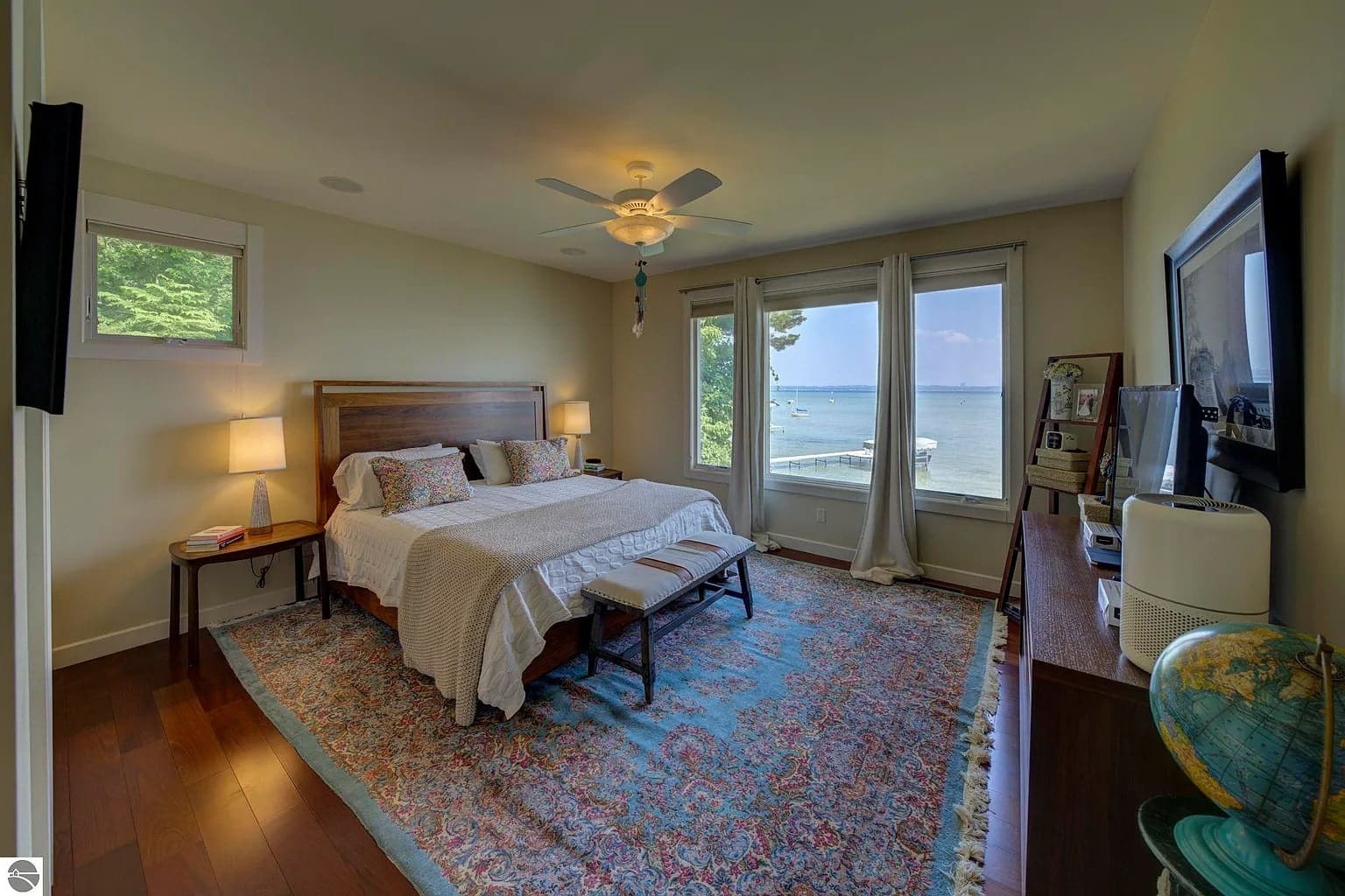 Bedroom with a large bed, colorful rug, and window view of a lake and trees.

