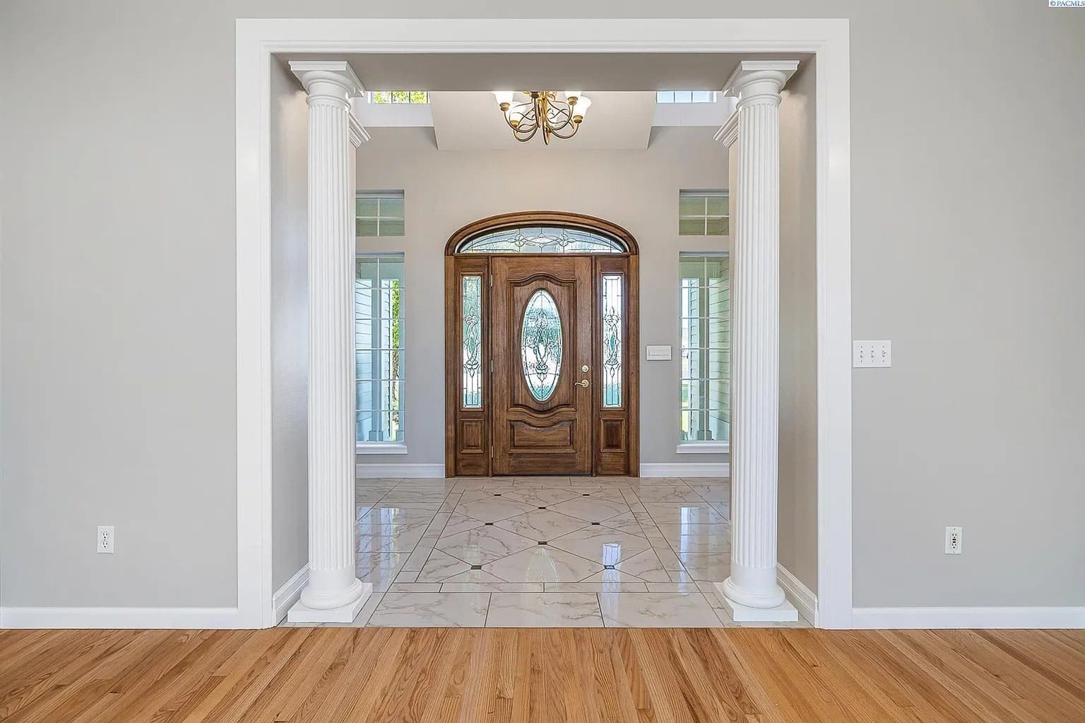 Elegant foyer with wooden double doors, marble flooring, and decorative columns.
