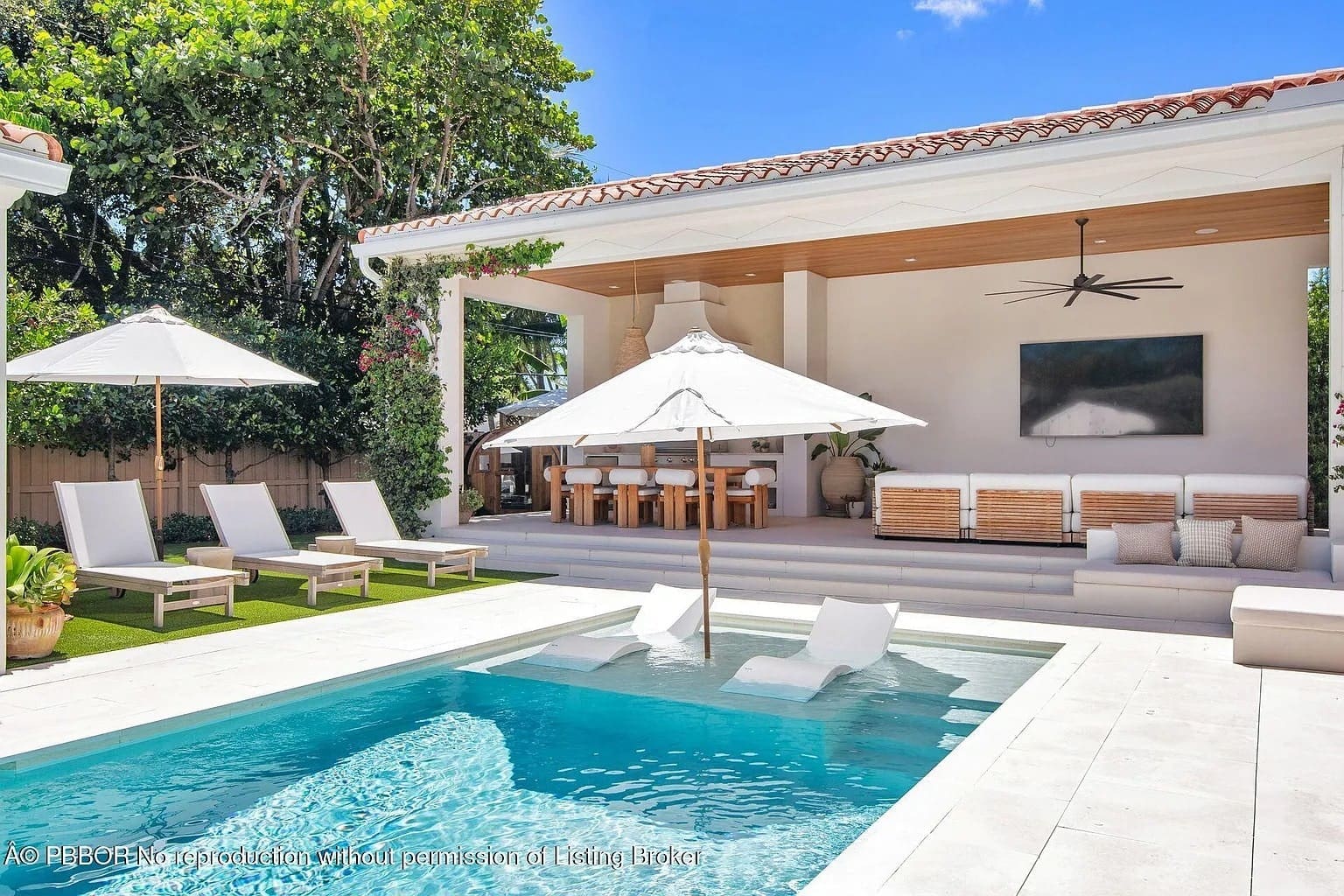 Luxurious outdoor patio with a pool, lounge chairs, umbrellas, dining area, and large TV.
