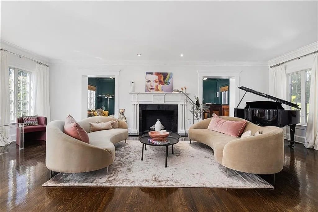Elegant living room with two curved sofas, a fireplace, a grand piano, and a portrait above.