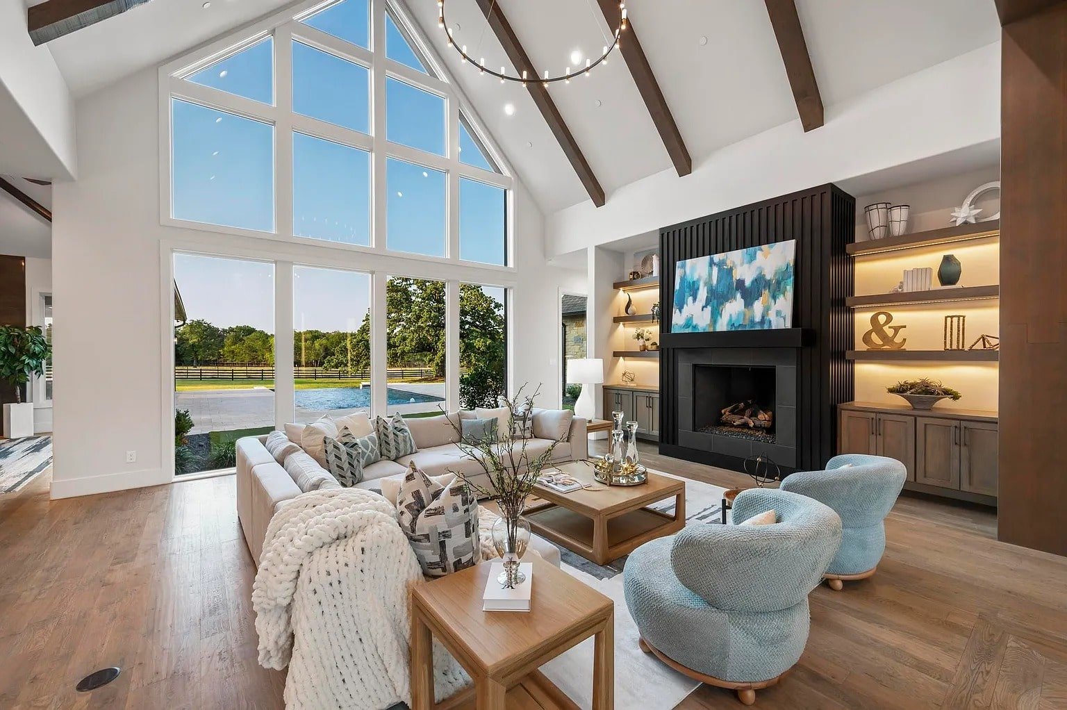Spacious living room with large windows, cozy seating, fireplace, and decorative shelves.