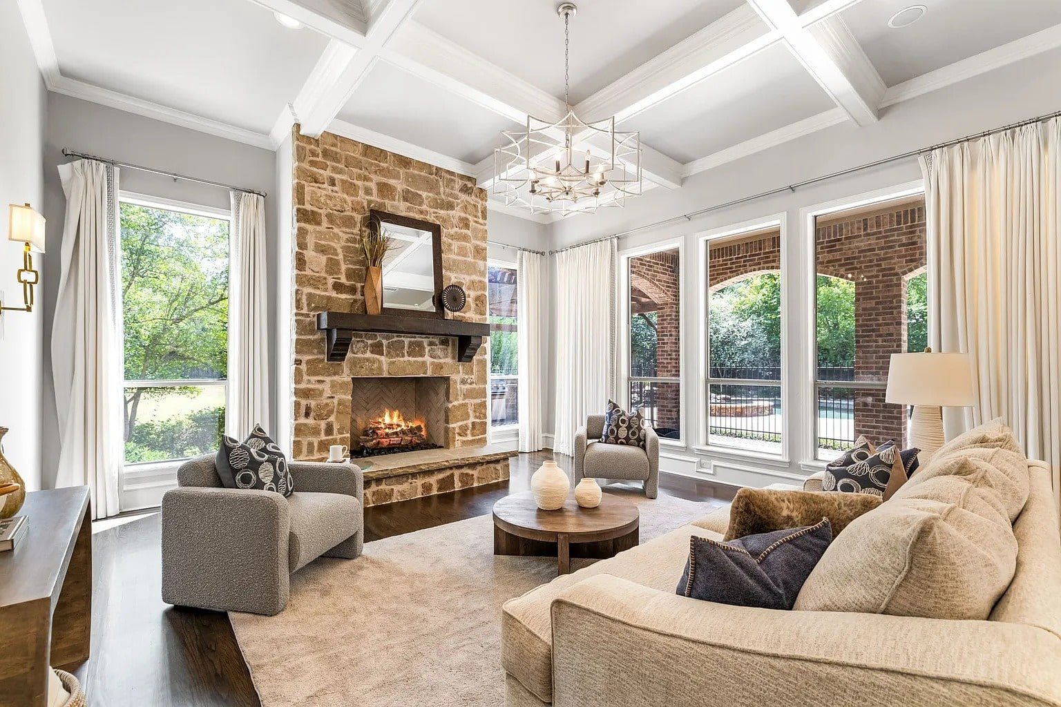 Cozy living room with stone fireplace, large windows, beige sofa, and modern chandelier.