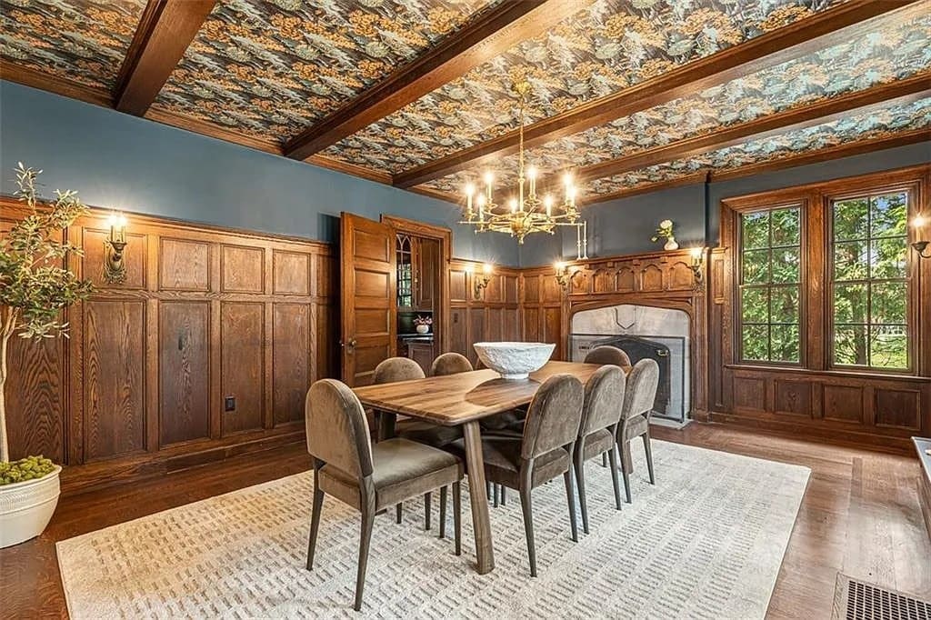 Dining room with wooden paneling, decorative ceiling, large windows, and a table with eight chairs.