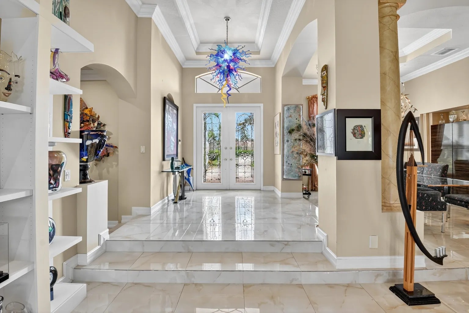 Spacious foyer with marble floors, colorful chandelier, and glass double doors leading outside.