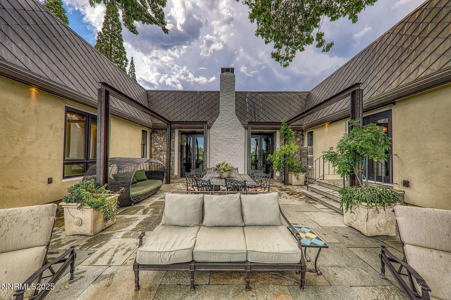 Spacious outdoor patio with seating, dining table, and greenery under a cloudy sky.