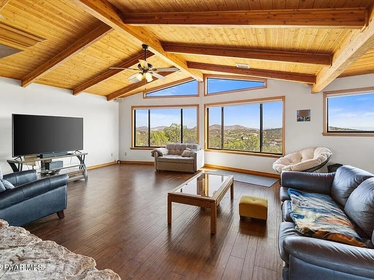 Spacious living room with wooden ceiling, large windows, sofas, and a TV. Scenic outdoor view.
