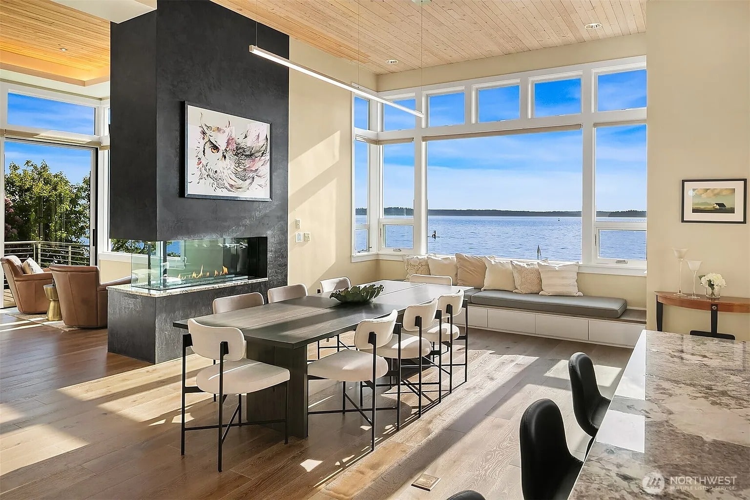 Modern dining area with large windows, lake view, fireplace, and contemporary furniture. Bright and spacious.