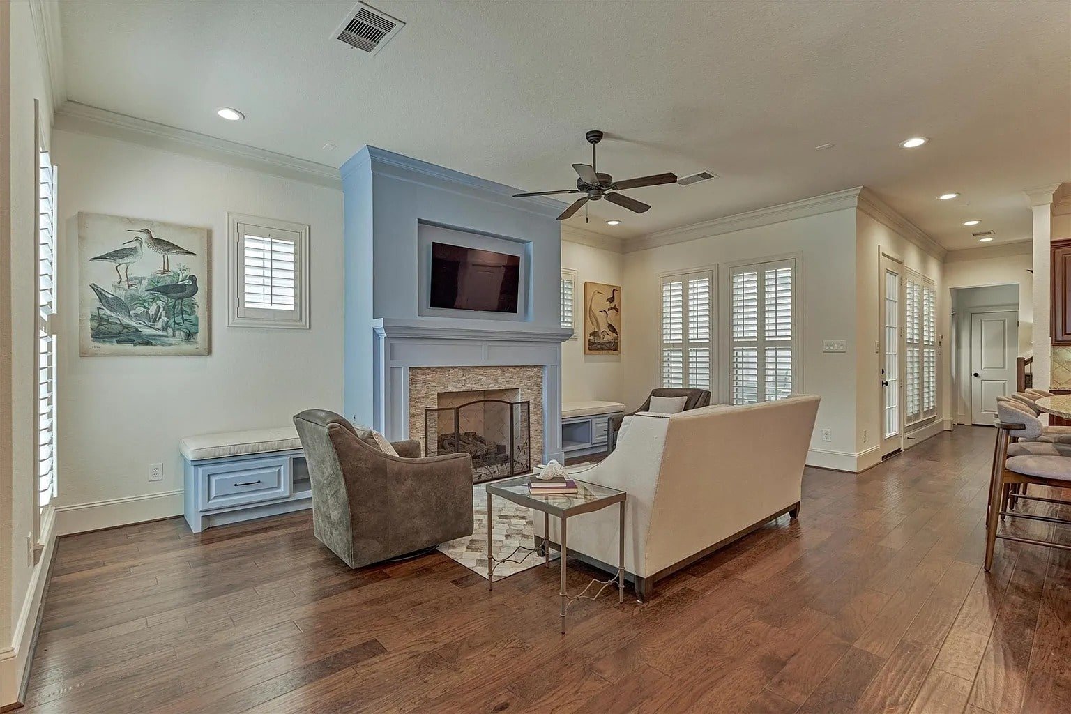 Living room with a fireplace, TV, sofa, armchair, and wooden flooring. Bright and cozy atmosphere.