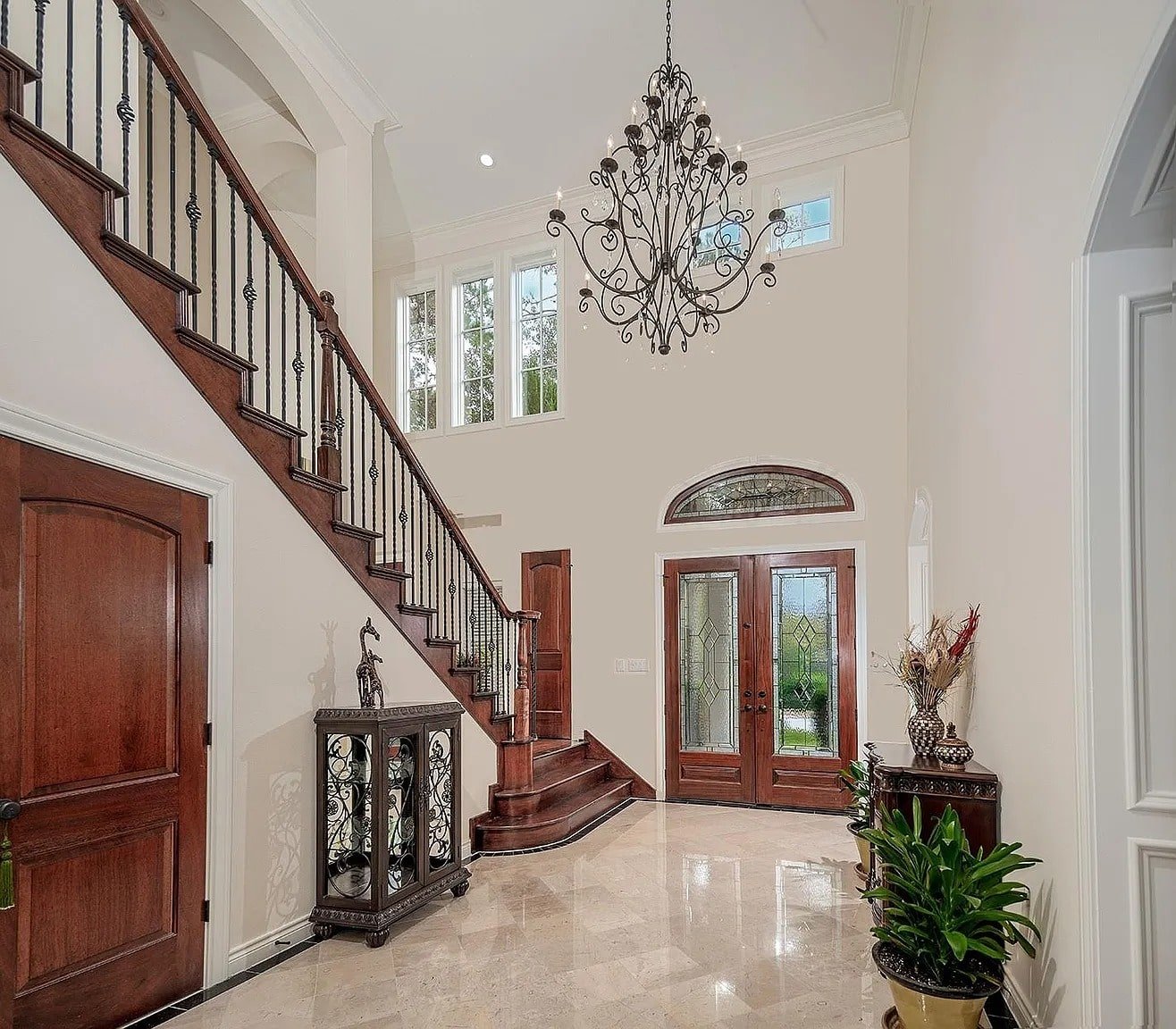 Elegant foyer with a grand staircase, chandelier, and wooden double doors.
