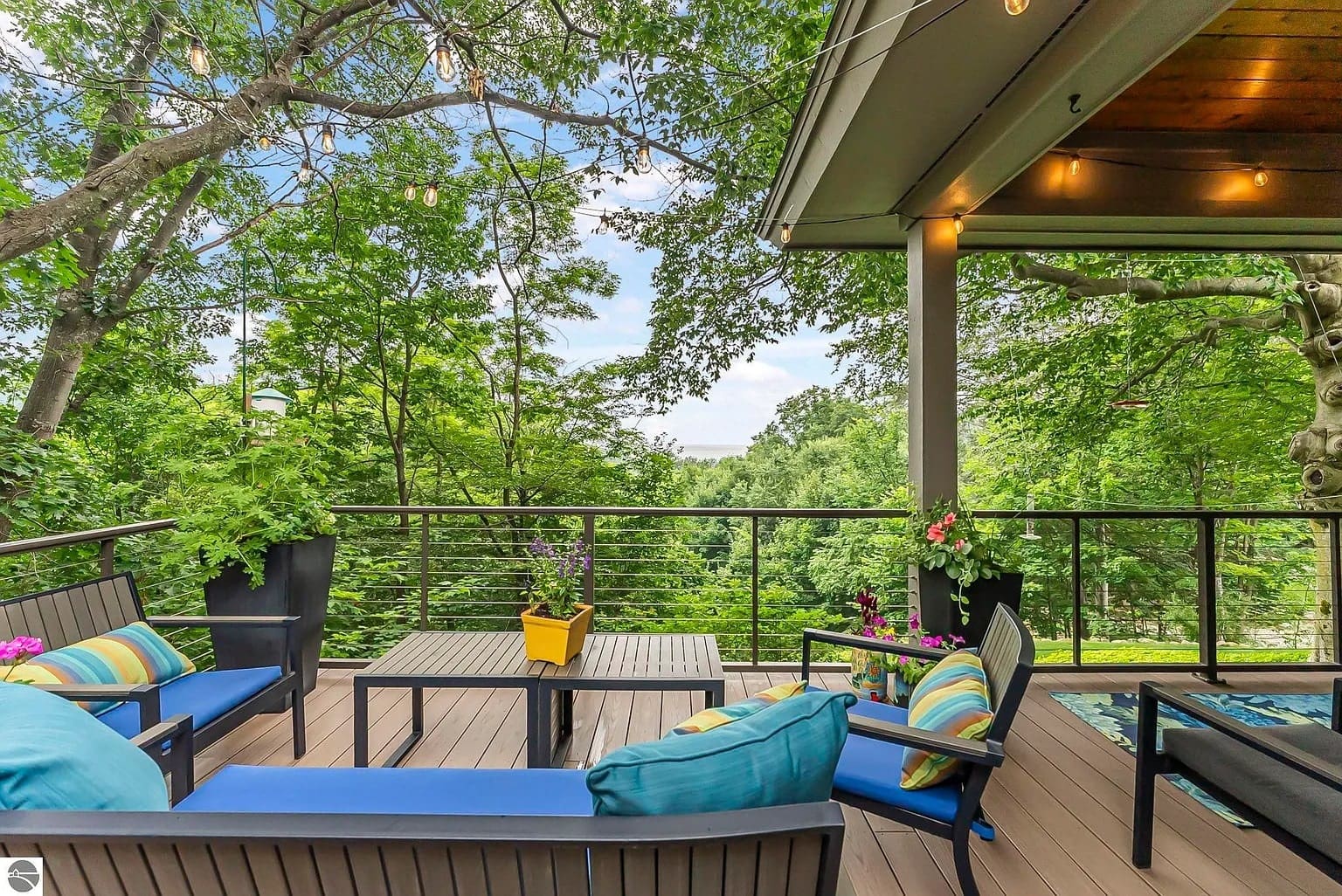 Outdoor patio with seating, colorful cushions, and potted plants, surrounded by lush greenery.