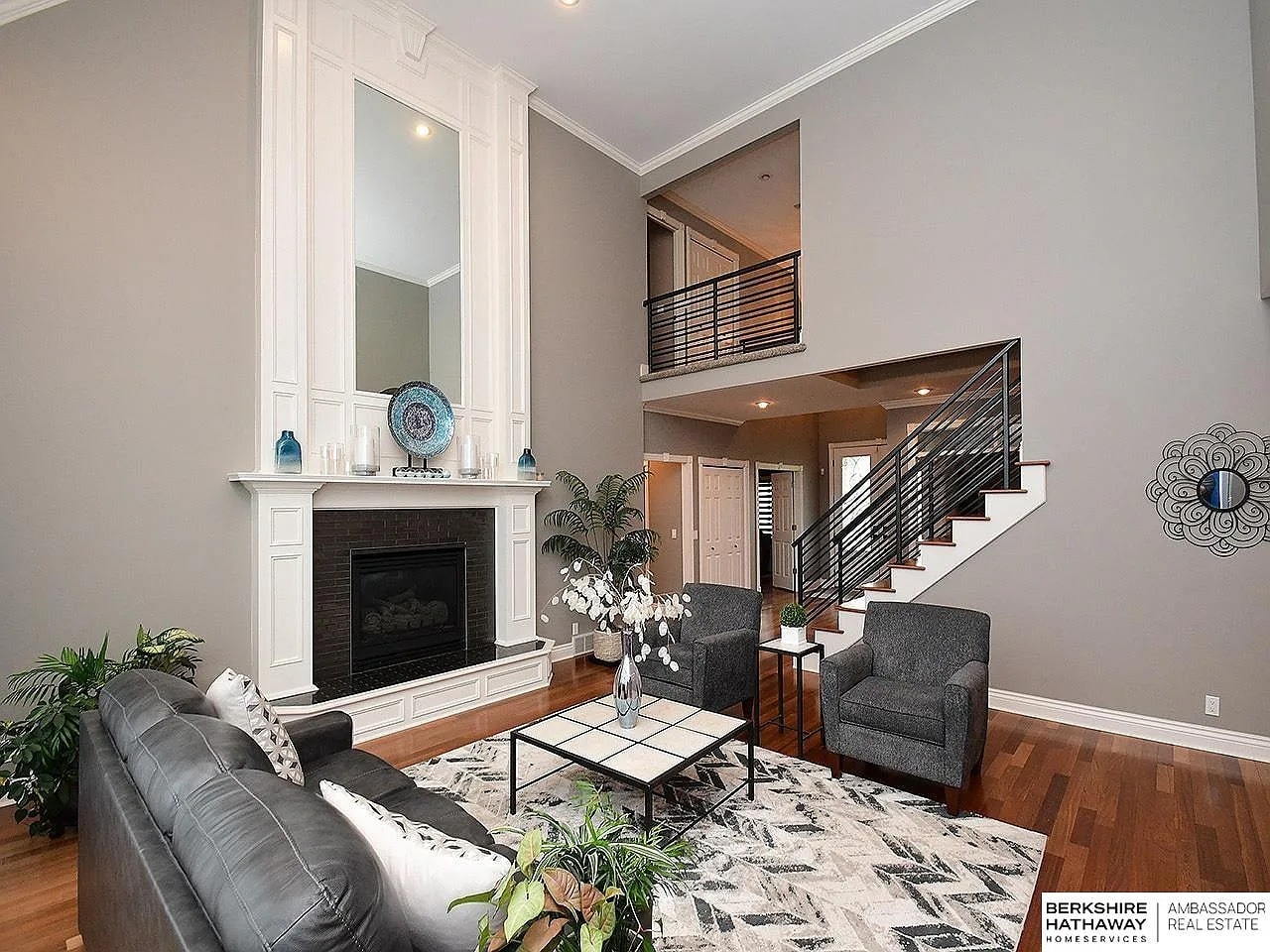 Modern living room with high ceiling, fireplace, gray furniture, and a staircase.