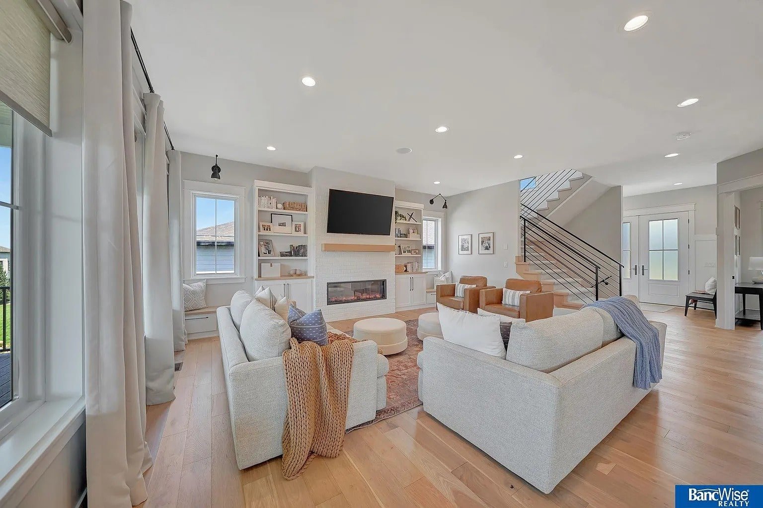 Modern living room with light wood floors, two sofas, a fireplace, and a wall-mounted TV.