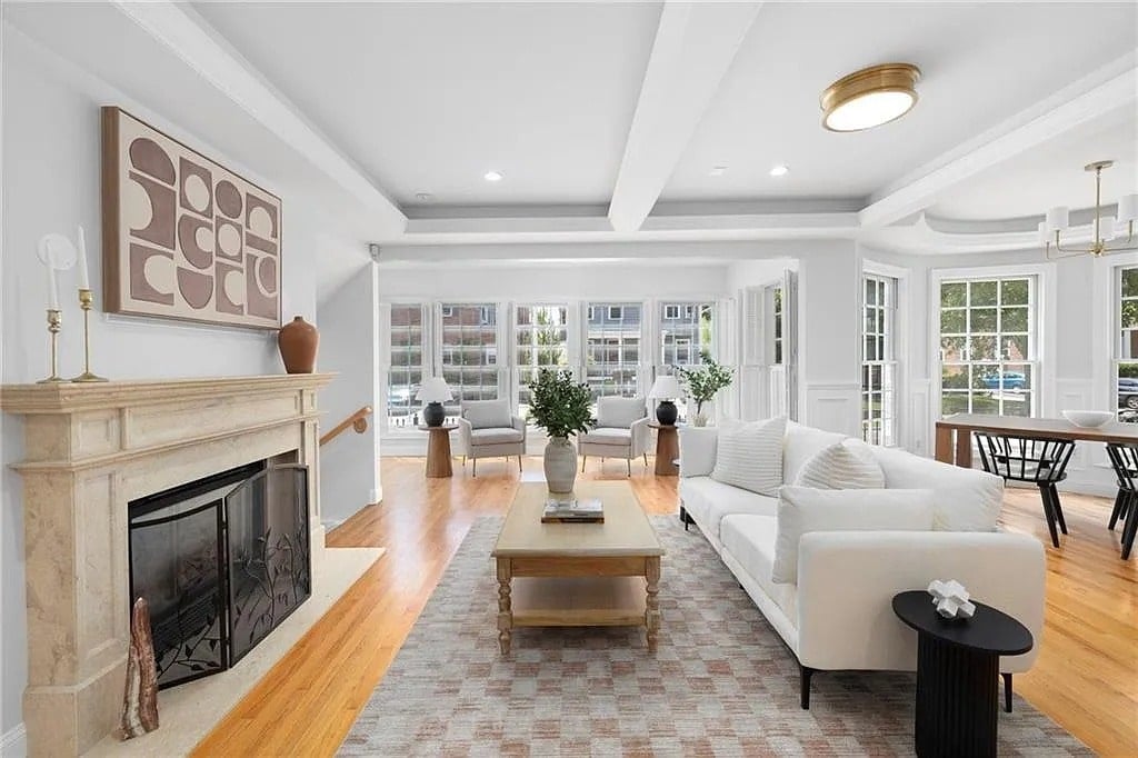 Spacious living room with white sofa, fireplace, large windows, and dining area in the background.