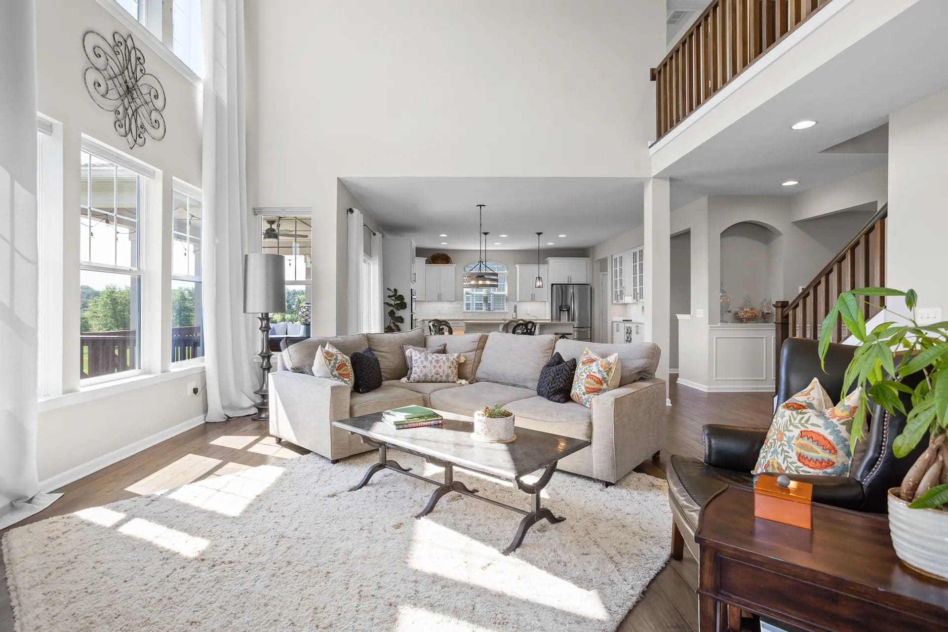 Spacious living room with large windows, gray sectional sofa, and open view to the kitchen.