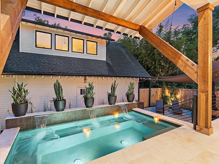 Outdoor pool area with modern design, potted plants, and a view of a house at sunset.