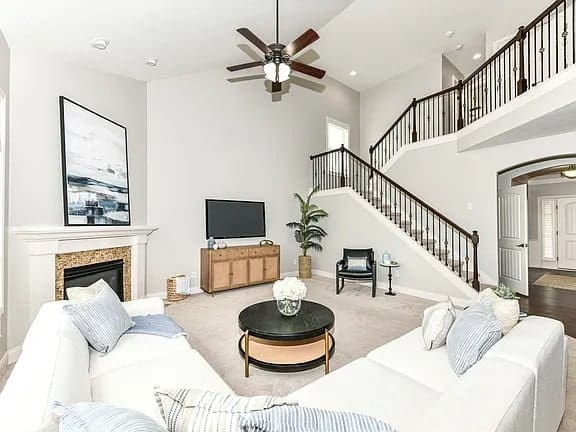 Spacious living room with white sectional sofa, TV, fireplace, and staircase with dark railings.