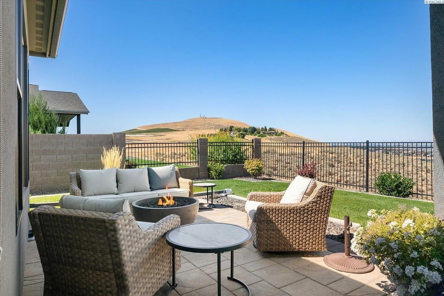 Patio with wicker furniture, fire pit, and scenic view of hills under a clear blue sky.