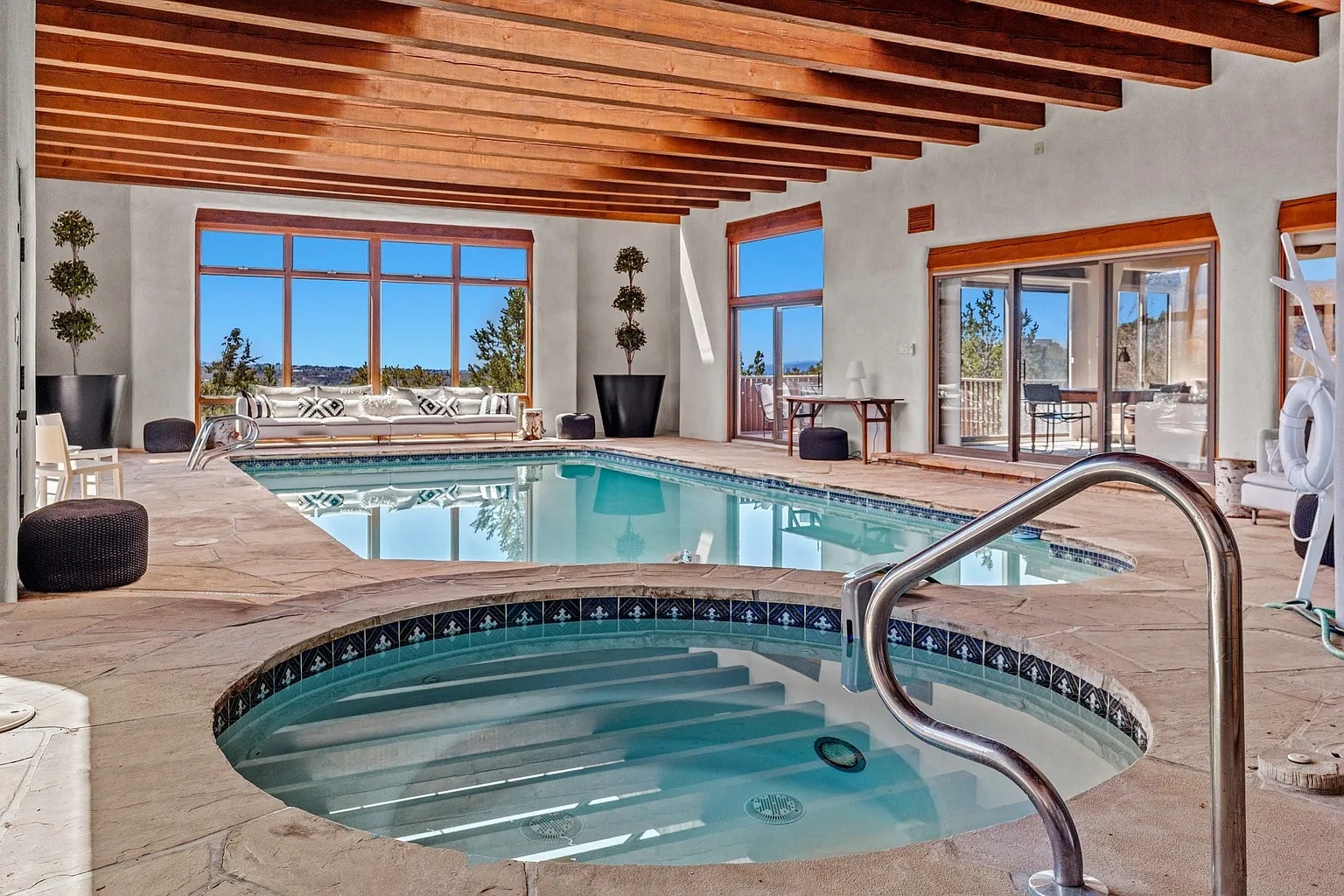 Indoor pool area with large windows, wooden ceiling beams, and a small hot tub in the foreground.