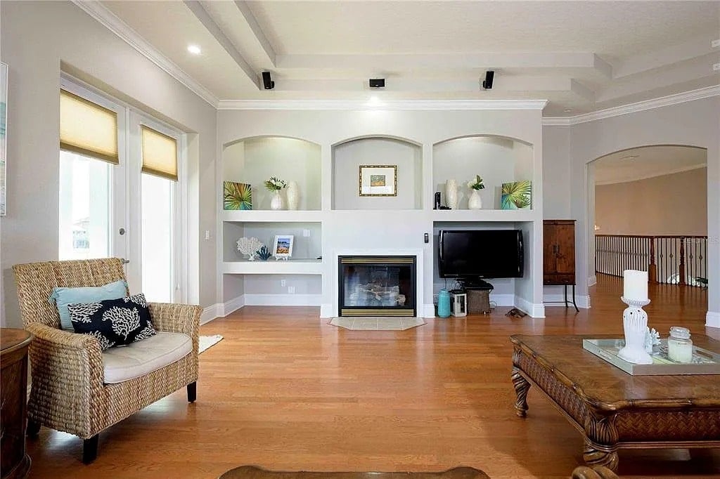 Spacious living room with a fireplace, TV, wicker chair, and decorative shelves.