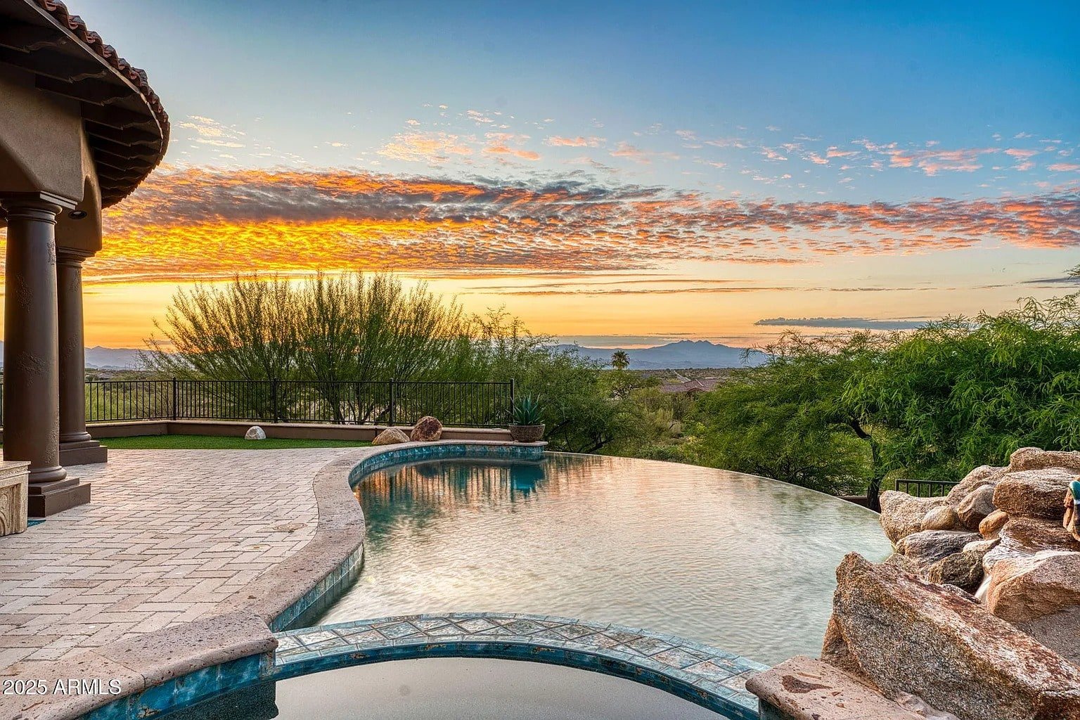 Infinity pool with a scenic sunset view, surrounded by trees and distant mountains.