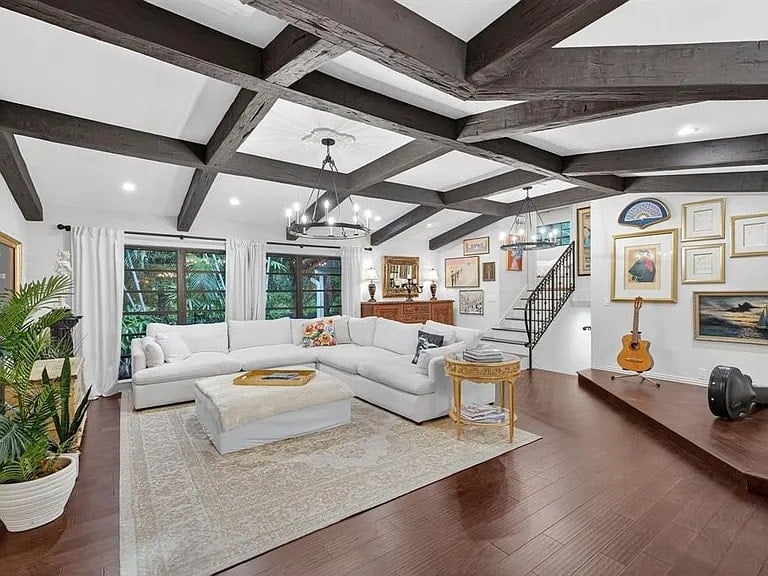Spacious living room with white sectional sofa, wooden beams, and eclectic wall art.