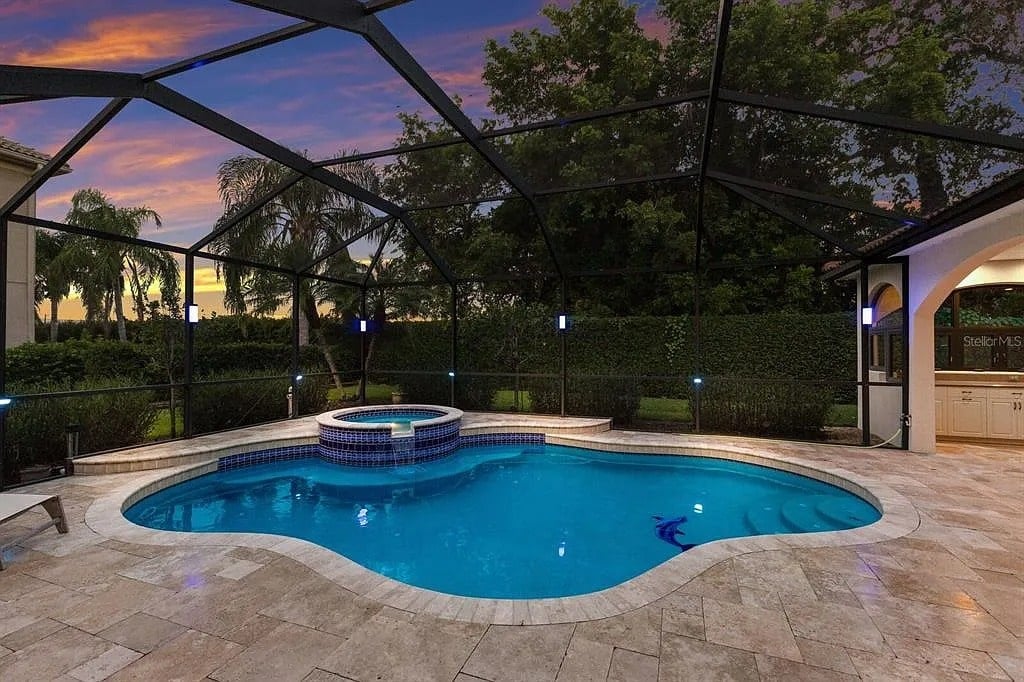 Outdoor swimming pool with attached hot tub, surrounded by a screened enclosure, at sunset.