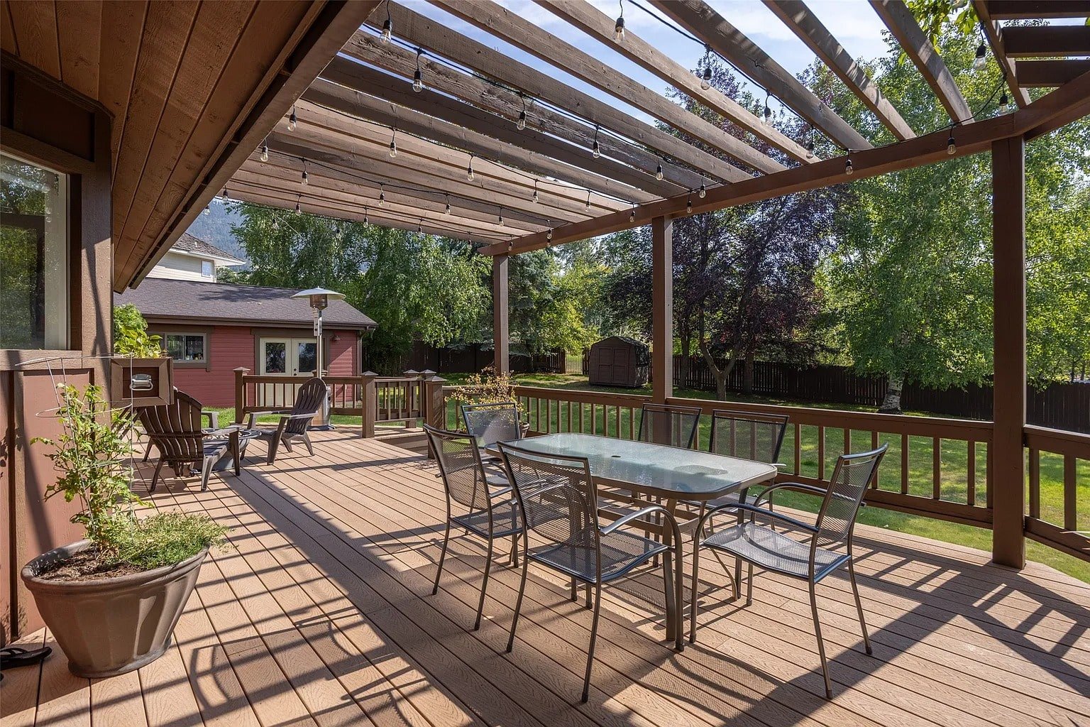 Spacious wooden deck with pergola, outdoor dining set, and view of a lush backyard.