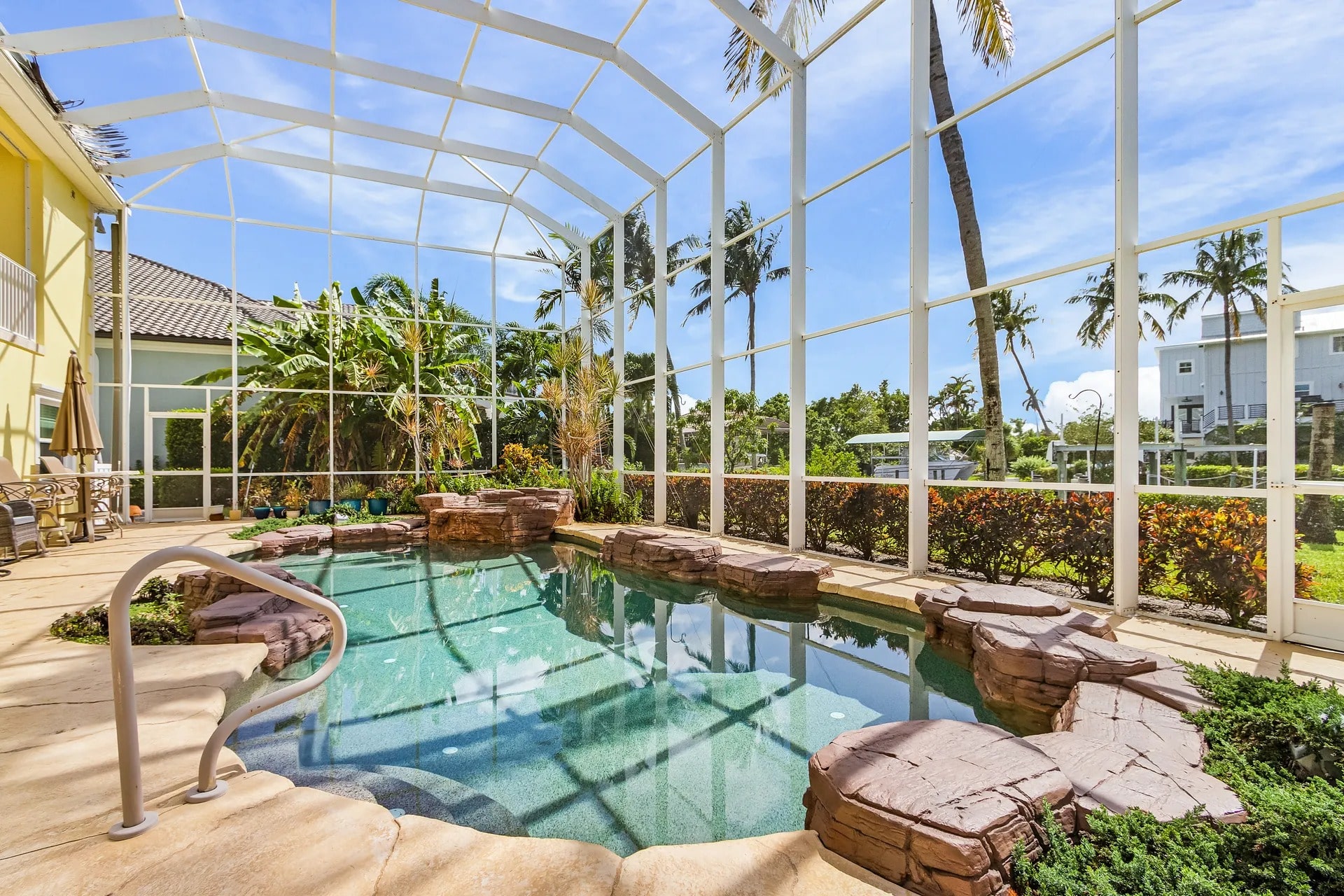 Enclosed outdoor pool with rock accents, surrounded by tropical plants and palm trees.